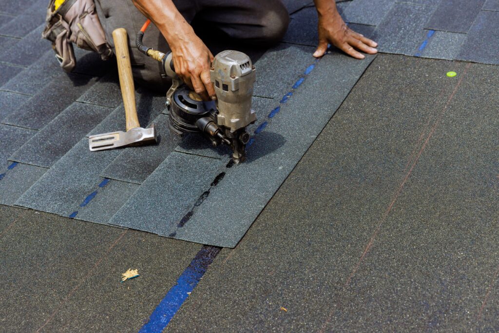 Roofer installing asphalt shingles with a nail gun, showing how long does it take to replace a roof.